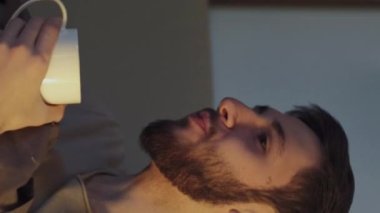 Dikey video. Televizyon akşamı. Ev tatili. Rahat bir adam, sabıka kanalı değiştiriyor, çay içiyor, karanlık bir gece odasında tek başına gülümsüyor, mavi ışıklı..