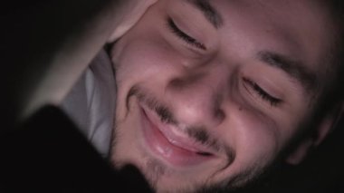 Dikey video. Yatak filmi. Gece aleti. Geç saatlere kadar boş vakit. Keyifli adam telefonda eğlenceli komedi programını izlerken karanlıkta yanıp sönen ışıkla gülümsüyor..