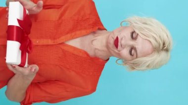 Dikey video. Küçük bir hediye. Hayal kırıklığına uğramış kadın. Hoşnutsuz bir durum. Üzgün kadın, elinde mavi poz veren kırmızı kurdeleyi tutan şüpheci duygularını ifade ediyor..