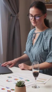 Dikey video. İş yorgunluğu. Bunalımlı çalışan. Uzaktan kumanda sorunu. Yorgun kadın ev işyerinde bir bardak şarap içmeyi bitirdi..