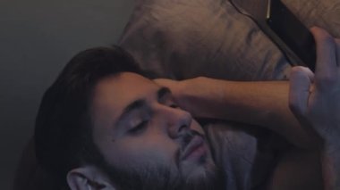 İnternet uykusuzluğu. Gece online. Gezici bağımlılık. Sıkıcı, uykulu, yorgun bir adam. Gece geç saatlerde, karanlık bir yatak odasında telefon kaydırağı kullanıyor..