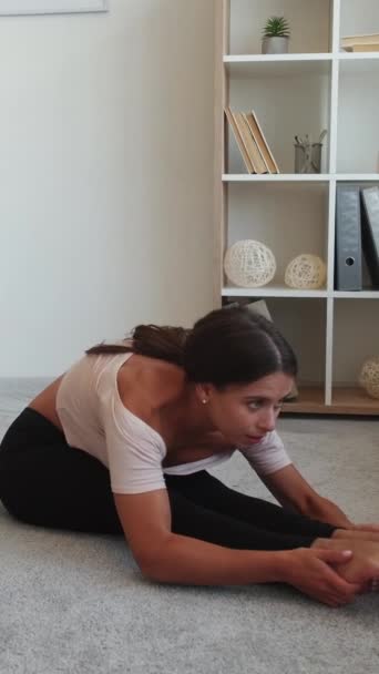 垂直ビデオ 前かがみだ Paschimottanasana運動 ヨガの本場 若いです柔軟な女性に座っている床の足一緒に手を前方に白い室内で — ストック動画