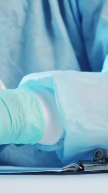 Dikey video. Klinik evrakları. Doktor reçetesi. Uyuşturucu kontrolü. Elleri eldivenli, ilaç şişkinlikleri inceleyen ve panoya notlar yazan bir tıp uzmanı..