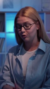 Dikey video. Online eğitim. Bayan öğretmenim. Sanal eğitim. Zeki, ilham verici kadın konuşan bilgisayar masasında karanlık neon ışıklı odada oturuyor..