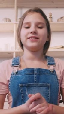 Dikey video. Çocuk video bloğu. İçerik çekimleri. Kendine güveni tam bir genç kız evde el kol hareketleri yaparak çevrimiçi blog için konuşma yapıyor..