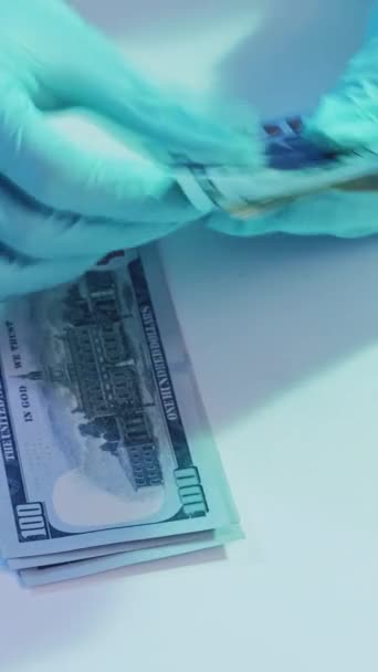 垂直录像 卫生保健工资 药品贿赂 医生们手戴蓝色防护手套 数着白桌上堆着的一百美元钞票 — 图库视频影像