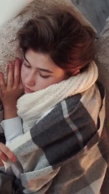 Dikey video. Hapşırma belirtileri. Mevsimsel grip. Hasta kadın kanepede yatarken soğuk algınlığı geçiriyor. Evde burun nezlesi geçiriyor..