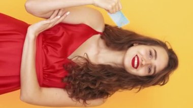Dikey video. İnternetten alışveriş. Kendine güvenen bir kadın. Meme ifadesi. Elinde kredi kartıyla öten, sarı düğümlü mutlu kadın..