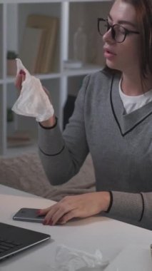 Dikey video. Yoğun bir iş. Hasta kadın. Mesafe iletişimi. Masada oturup dizüstü bilgisayarla konuşan, cep telefonu hapşıran, peçete odası aydınlatması yapan yorgun bir kadın..