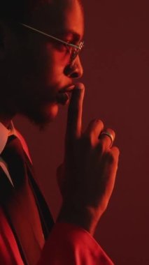 Dikey video. Sessiz ol. Gizli komplo. Zarif smokinli beyefendinin parlak kırmızı profili gözlüklü parmak yüzüğü uyarısı, koyu renk jestli..