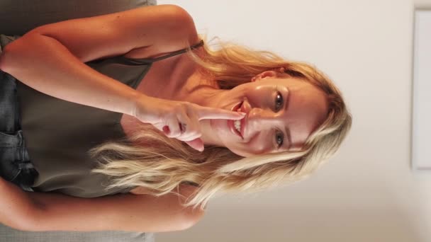 垂直ビデオ 秘密を守るんだ 静かな女性 顔の表情 笑顔女性でカジュアルルック保持シャープな指で口の中に光の部屋のインテリア — ストック動画
