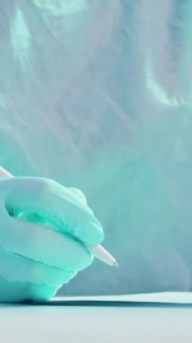 Dikey video. İlaç kayıtları. Hemşire evrakları. Elleri koruyucu eldivenlerde olan tıp uzmanı beyaz masadaki kayıt belgelerindeki bilgileri kontrol ediyor..