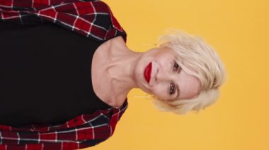 Dikey video. Kadınsı güç. Güzel kadın. Şık, orta yaşlı, sarışın kadın kırmızı ruj. Sarı poz veriyor..