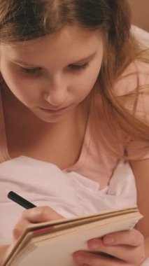 Dikey video. Çocuk günlüğü. Yaratıcı hobi. Çocuk hayal kuruyor. Eskiz defterinden ilham alan kız, sabahları evde rahat beyaz bir battaniyenin içinde dinleniyor..