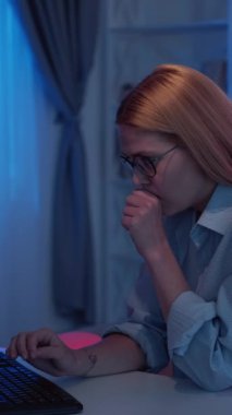 Dikey video. Mesafe çalışması. Yorgun bir kadın. Çevrimiçi araştırma. Karanlık neon ışıklı odada geç saatlere kadar çalışan, bilgisayar klavyesinde çalışan yorgun bayan..