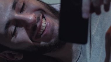 Dikey video. Film uygulaması. Gece keyfi. Çevrimiçi eğlence. Neşeli adam cep telefonu uygulamasını gülerek eğlenceli komedi programı izliyor..