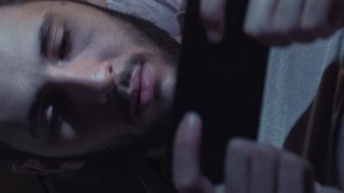 Dikey video. Gezici oyun. Gece keyfi. Uykusuzluk teknolojisi. Yatakta cep telefonu kullanan yorgun ve huzursuz bir adam..