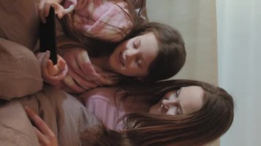 Dikey video. Aile aleti. Ev tatili. Dijital hafta sonu. Rahat anne kız, sabah yatak odasında telefonda çizgi film izlemekten zevk alıyor..
