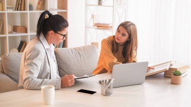 Akademik destek. Ev öğretmeni. Sınav için hazırlanan öğretmeniyle birlikte aydınlık odada oturma masasında ders veriyor..