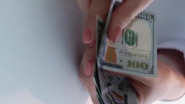 Dikey video. Nakit para. Banka hesabı. Finansal depozito. İş kadınlarının eli beyaz arka plandaki 100 dolarlık banknotları kredi kartıyla sayıyor..