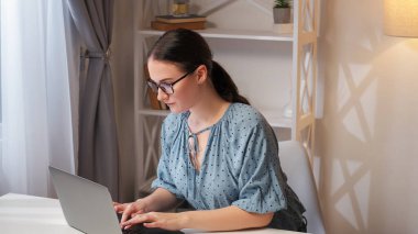 Uzaktan kumanda. İnternet araştırması. Çevrimiçi yönetim. Çalışan akıllı, meşgul bir kadın, evde çalışıyor. Modern işyeri iç mekanında dizüstü bilgisayar kullanıyor..