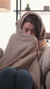 Dikey video. Enfeksiyon kapmış. Hasta kadın. Evde iyileşme. Acı çeken kadın, kareli kanepeye sarılı, hapşıran peçete, kendini kötü hissediyor..