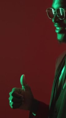 Dikey video. Cesaret verici bir jest. İyi iş çıkardın. Onaylanmış bir hayranlık. Yeşil, neon ışıklı, zarif takım elbiseli adam baş parmağıyla işaret ederek saygı gösteriyor..