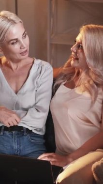 Dikey video. Aile web taraması. İnternetten alışveriş. Anne kız dizüstü bilgisayarla konuşuyor internetten alışveriş yapıyor akşam odasındaki koltukta oturup tartışıyor..