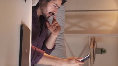 Dikey video çağrısı. Çevrimiçi sohbet. Mesafe iletişimi. Rahat adam cep telefonu kamerasıyla konuşuyor modern evdeki koltukta yatıyor..