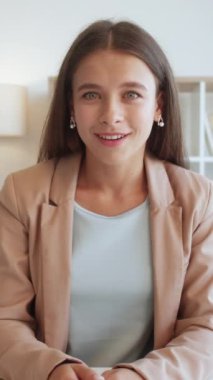 Dikey video. Çevrimiçi iletişim. İçten bir sevinç. Terapi desteği. Duygusal olarak şaşırmış, iş elbisesi içinde gülümseyen, el kol hareketi yapan, içten içe duygularını ifade eden bir kadın..