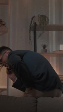 Dikey video. Mobil iletişim. Mutlu adam. Hoş bir karar. Takım elbiseli, akıllı telefondan konuşan esinlenilmiş adam karanlık odanın içinde koltukta oturuyor..
