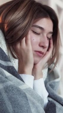 Dikey video. Baş ağrısı semptomu. Grip oldum. Battaniyeye sarılı sağlıksız bir kadın. Şakaklarına masaj yapıyor. Acı çekiyor..