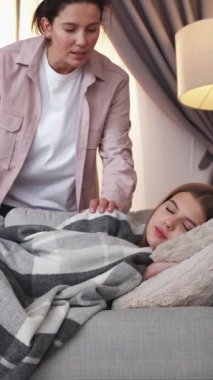 Dikey video. Evde şekerleme. Uyan kızım. Genç kızı uyandıran kadın hafta sonu ekoseli kanepenin altında uyuyor..