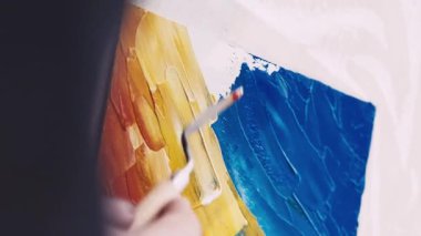 Dikey video. Sanat eseri yaratımı. Kadın ressam. İç mekan resmi. Tanımlanamayan bir kadın, renkli spatula resimleriyle tuvale soyut bir manzara çiziyor..