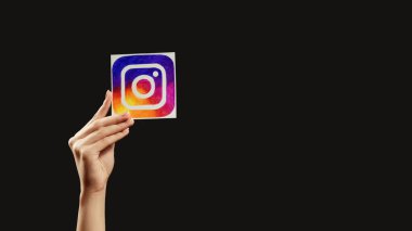 Kharkiv, Ukrayna - 12 Mayıs 2020: Instagram 'ı takip et. Küresel iletişim Sosyal medya uygulama simgesini tutan kadın el koyu boş arkaplanda izole edilmiş.