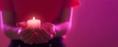 Mum meditasyonu. Azizler Günü. Dua geleneği. Kadın ellerinin parlak pembe neon arka planda yanan mum ışığını tuttuğu yakın plan geniş afiş.
