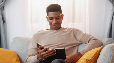 Roman okuyorum. Edebiyat hobisi. Ev tatili. Çok satan kitaplardan hoşlanan mutlu, heyecanlı genç adam oturma odasındaki rahat kanepede dinleniyor..