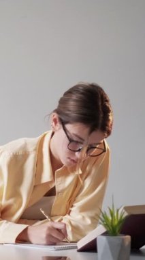 Dikey video. Not öğrenci. Özet yazıyorum. Çalışan kız, iş yerinde boş alan olan gri duvarla ilgili yeni bilgiler okumakla meşgul..