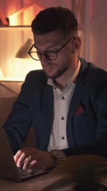 Dikey video. Online eğitim. Erkek öğretmen. Ders hazırlığı. Masanın üzerinde karanlık odanın içinde açık kitaplarla dizüstü bilgisayarı yazan konsantre bir adam..