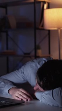 Dikey video. Amatör. Uyuyan adam. Dijital teknoloji. Yorgun adam dizüstü bilgisayar içerideki aydınlık gölge odasını gösterirken el üstünde oturuyor..