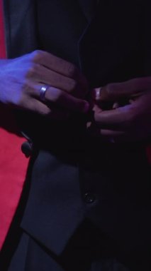 Dikey video. Centilmen tarzı. Şık bir moda. Lüks parti görünüşü. Neon ışığı tanınmayan adam koyu mor üzerine kırmızı şık smokin ilikliyor..