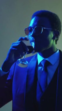 Dikey video. Centilmen partisi. Neşeyi kutluyoruz. Disko eğlencesi. Kırmızı gözlüklü neon ışıklı adam konfeti yağmuru dumanında şarap içerek dans etmekten zevk alıyordu..