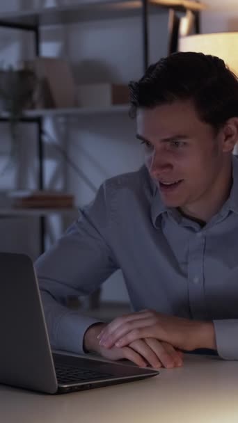 垂直录像 令人震惊的电影 奇怪的男人 在线翻译 忧心忡忡的家伙看着笔记本电脑 饶有兴致地坐在写字台的光影里面 — 图库视频影像