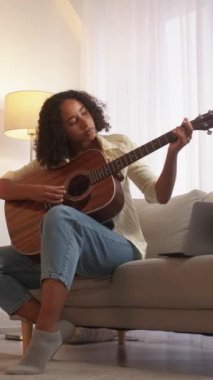 Dikey video. Şarkı öğrenme. Gitar çalıyor. Müzik hobisi. Odaklanmış kadın müzisyen akustik enstrüman üzerinde akorlar çalışıyor..