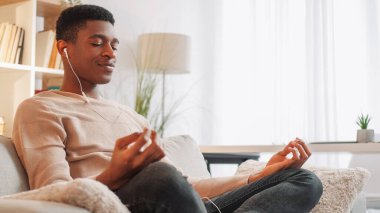 Ev meditasyonu. Yoga sakinliği. Ses rahatla. Rahatlık ve rahatlık. Huzurlu sakin bir adam. Kulaklıkla soğuk müzik dinliyor. Oturma odasındaki rahat koltukta poz veriyor..