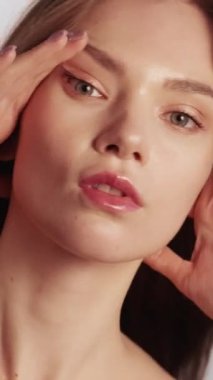 Dikey video. Güzellik modası. Profesyonel fotoşop. Çıplak makyajlı, parlak tenli, kendine güvenen model kadın gri arka planda ışık altında kozmetik reklamlar için poz veriyor..