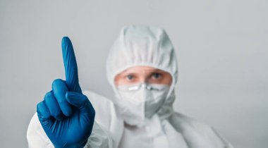 Doktor uyarısı. Sağlık uzmanıyım. Beyaz koruyucu ekipman maskeli kadın virolog eldivenler dikkat el işareti gri arka planda izole.