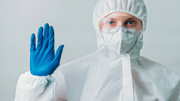 Stop pollution. Technological disaster. Protection suit. Woman scientist specialist in white coverall ppe gloves raised hand sign isolated on grey background.