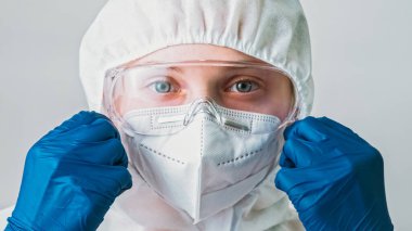 Hava kirliliği. Ekolojik felaket. Solunum koruması. Mavi eldivenli kadın bilim adamı gri arka planda izole edilmiş beyaz yüz maskesi takıyor..