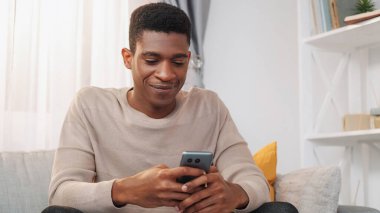 Gezici eğlence. Gadget sohbeti. İnternet taraması. Akıllı telefondan mesaj atan mutlu, rahat adam evde internet üzerinden iletişimin keyfini çıkarıyor..